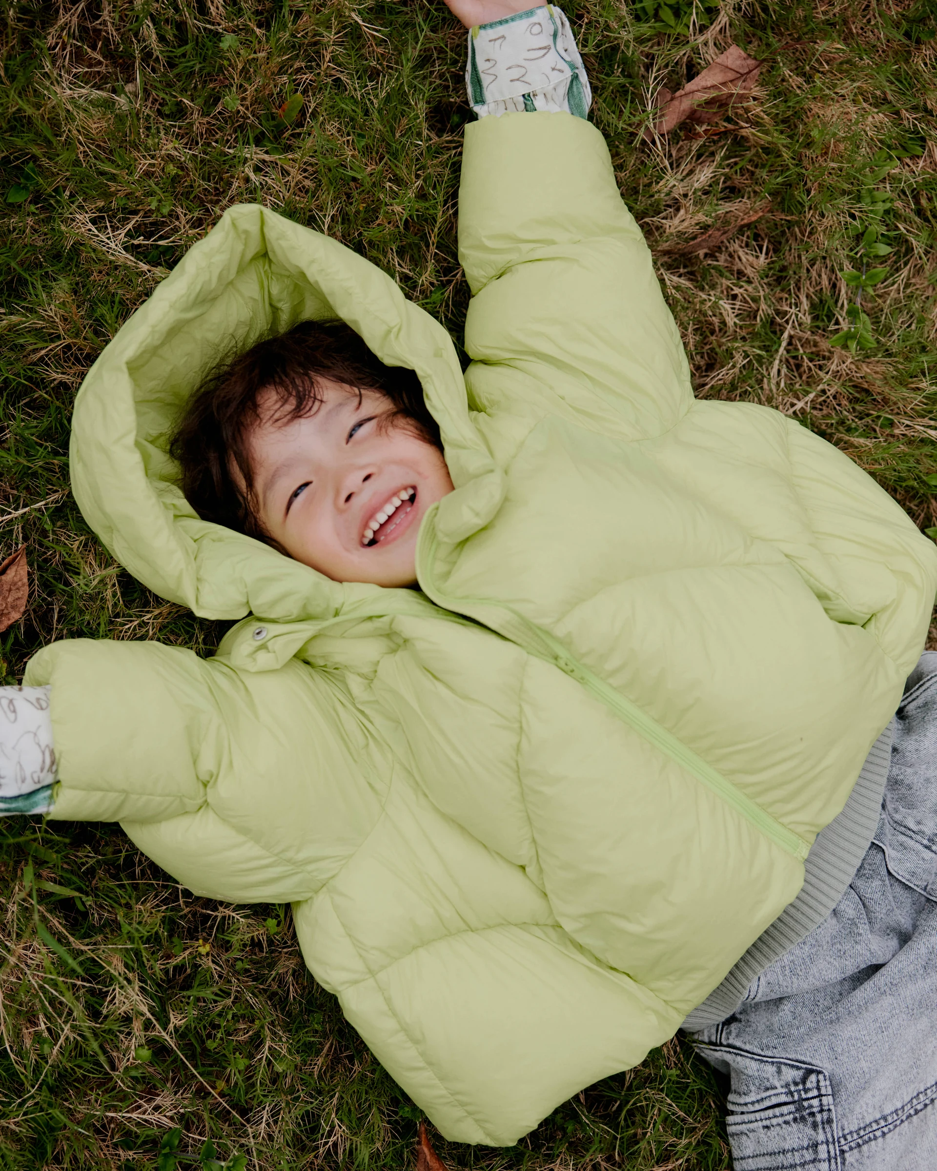 Child lying on the grass in a pale green jnby by JNBY puffer jacket