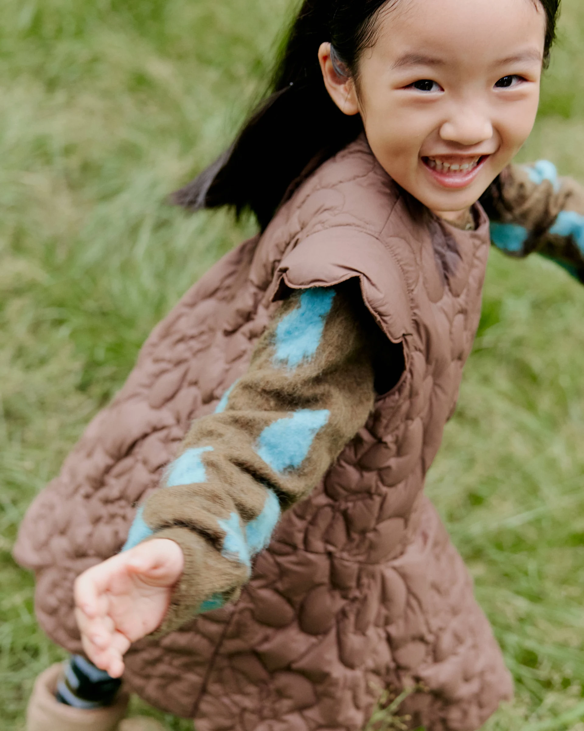 Smiling girl reaching toward the camera in jnby by JNBY clothing