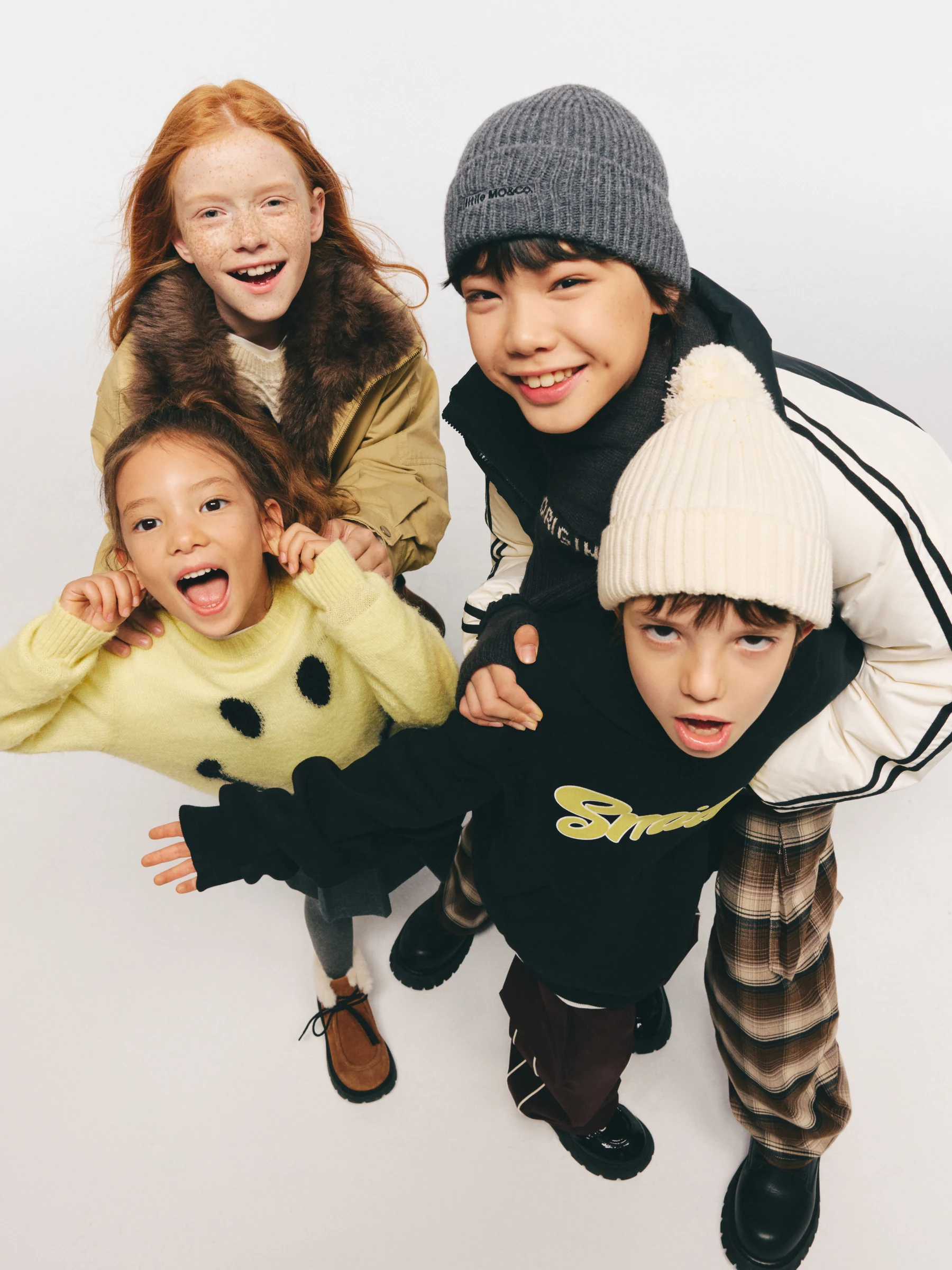 Four children posing together in little MO&Co. knitwear and outerwear