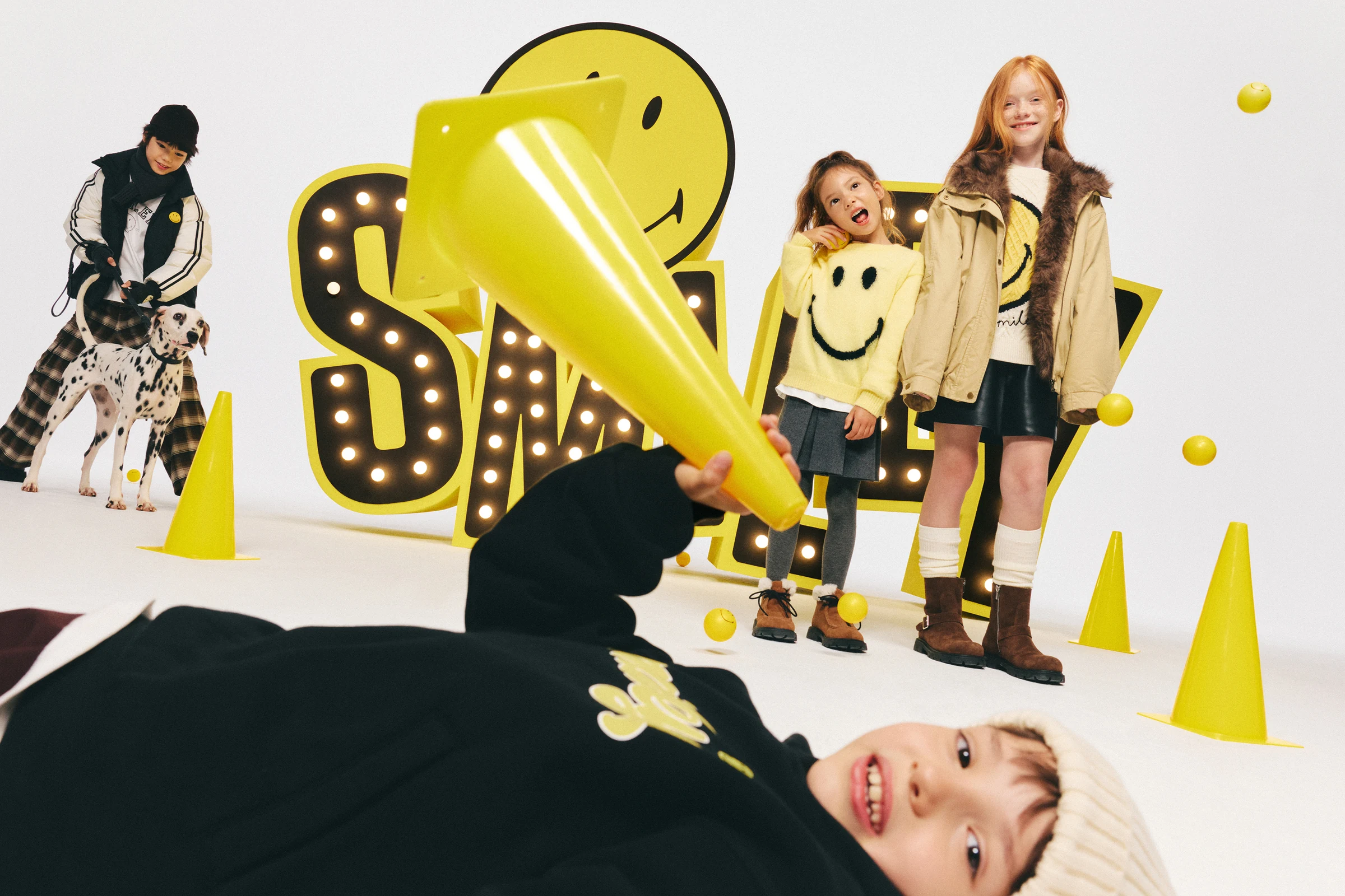 Children playing among yellow smiley props and cones with a dog