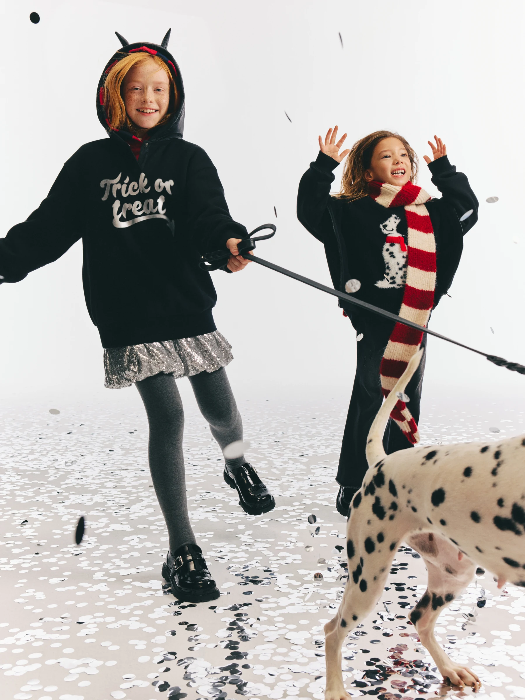 Two children playing in dark graphic outfits with a spotted dog