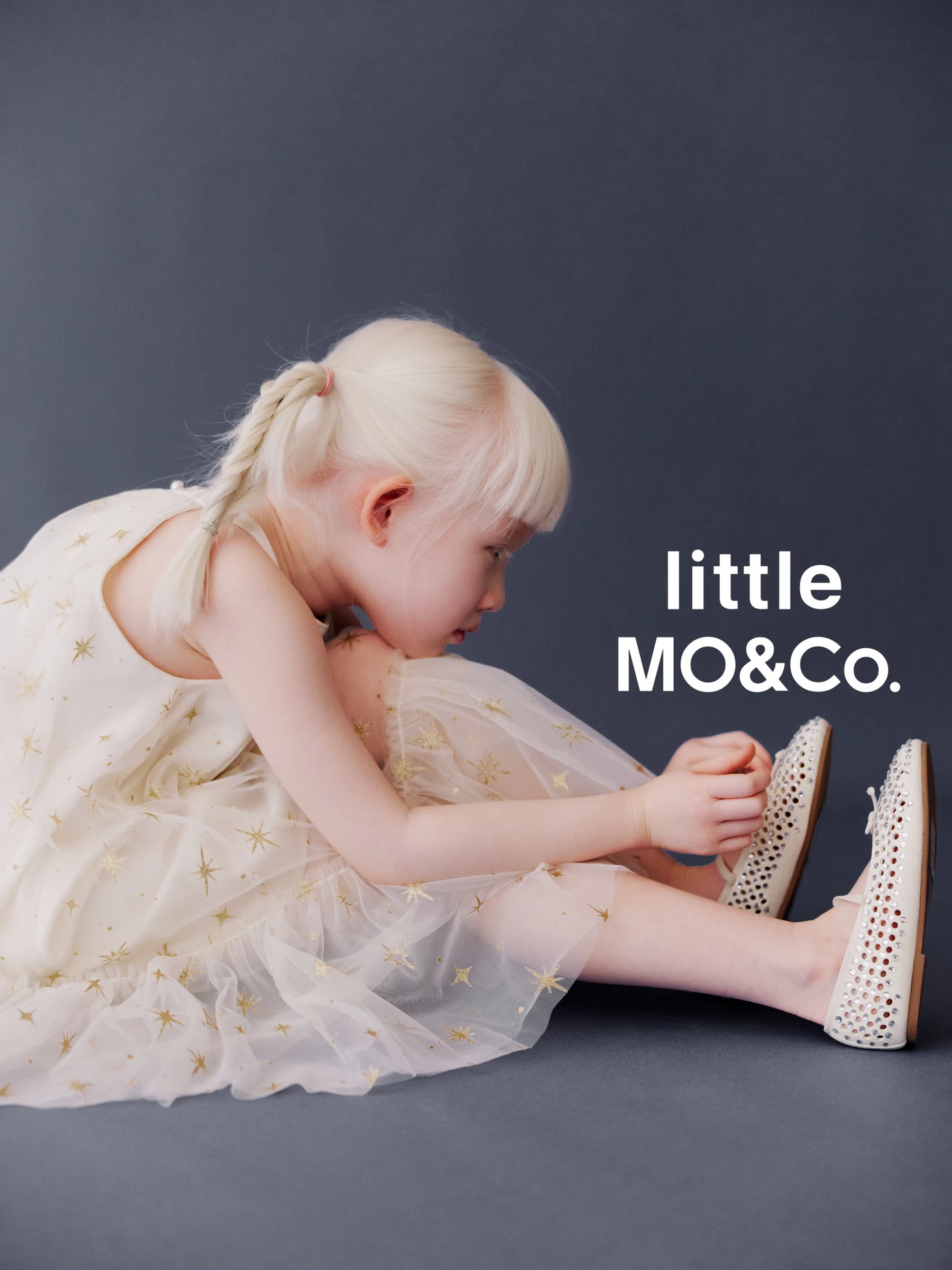 Child in a star-pattern dress adjusting a sparkling shoe