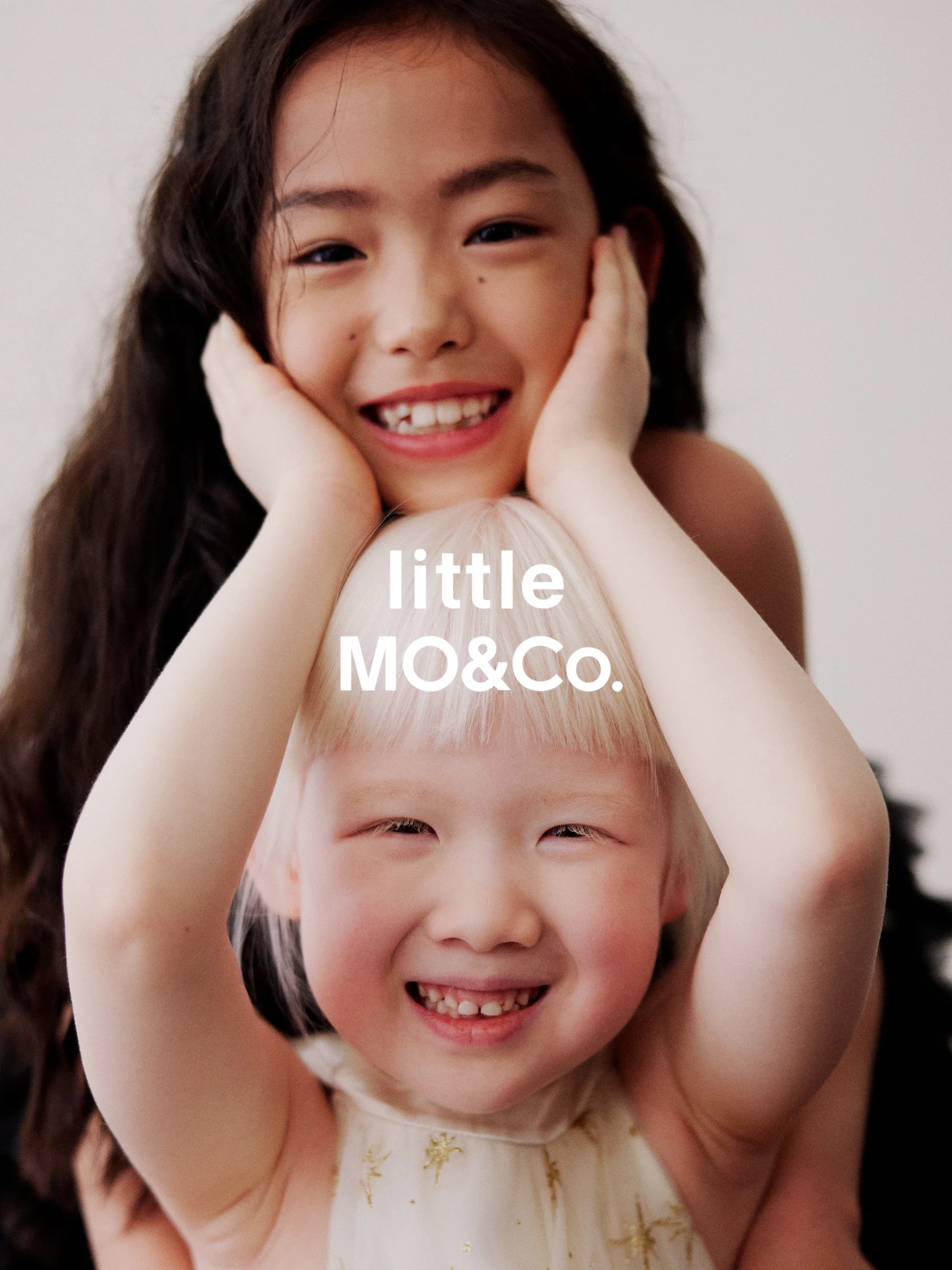 Two smiling girls posing together for little MO&Co.