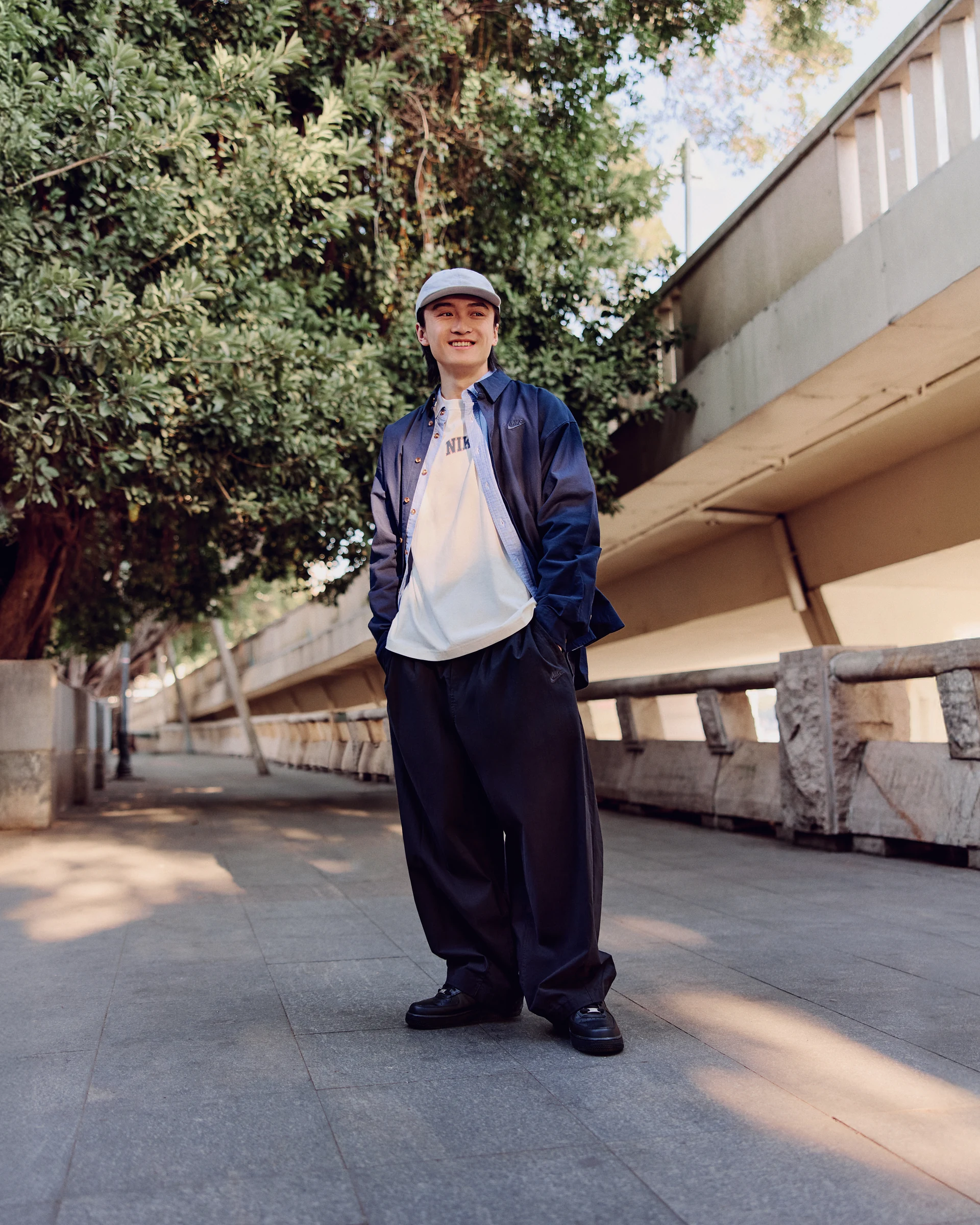 NIKE streetwear portrait beside trees and a concrete railing